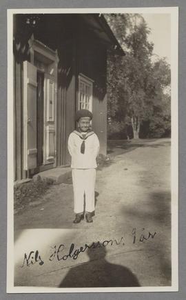Den unge pojken Nils Holgersson stående framför hus, iklädd sjömanskostym